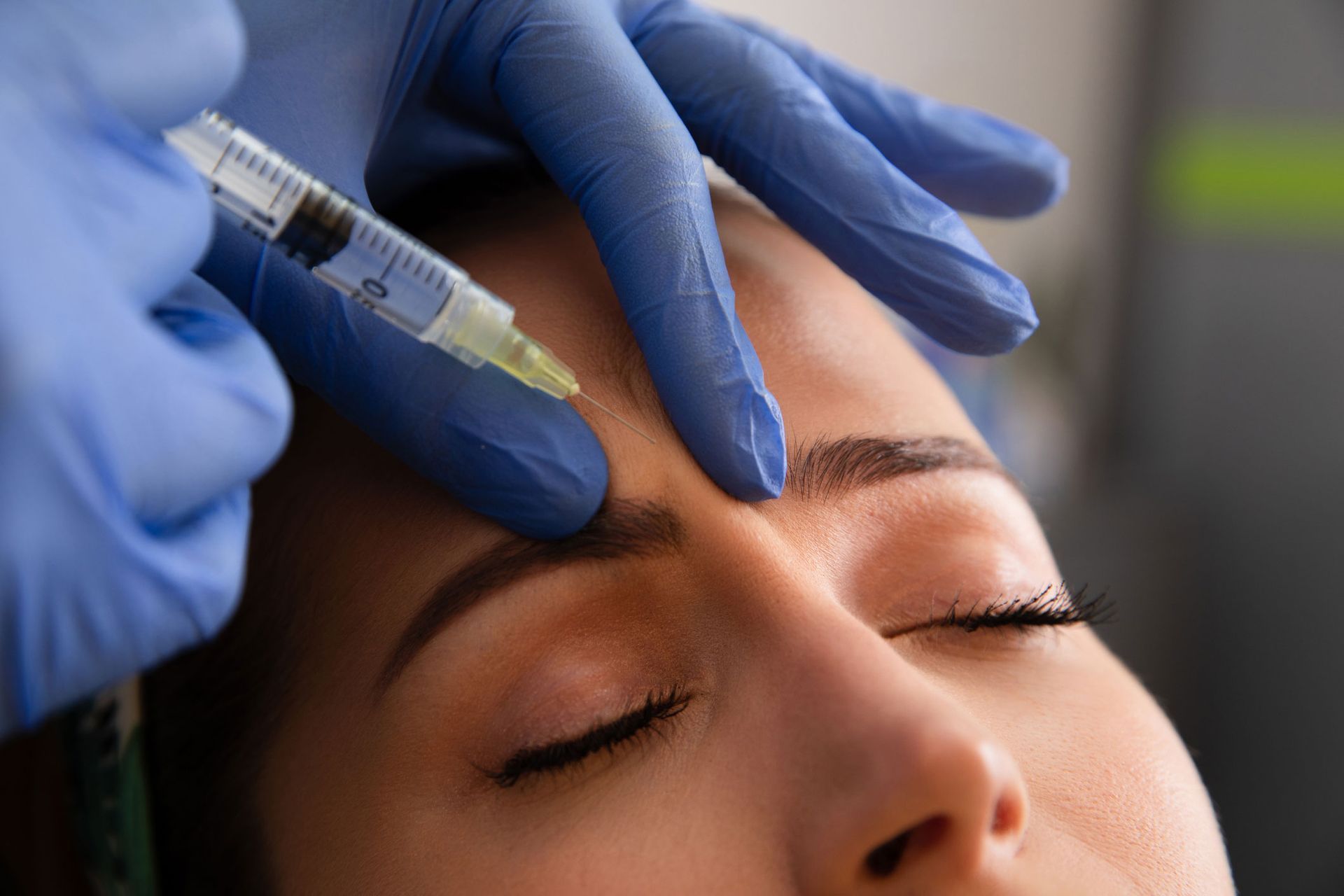 Gloved hand injecting brow. Woman with closed eyes receiving cosmetic procedure in clinic.