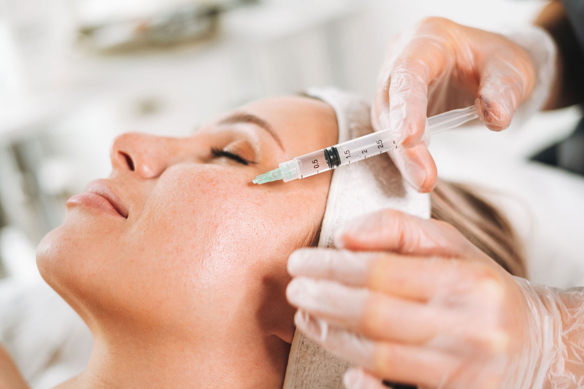 Person receiving facial injection in a medical setting. A gloved hand injects the cheek near the eye.
